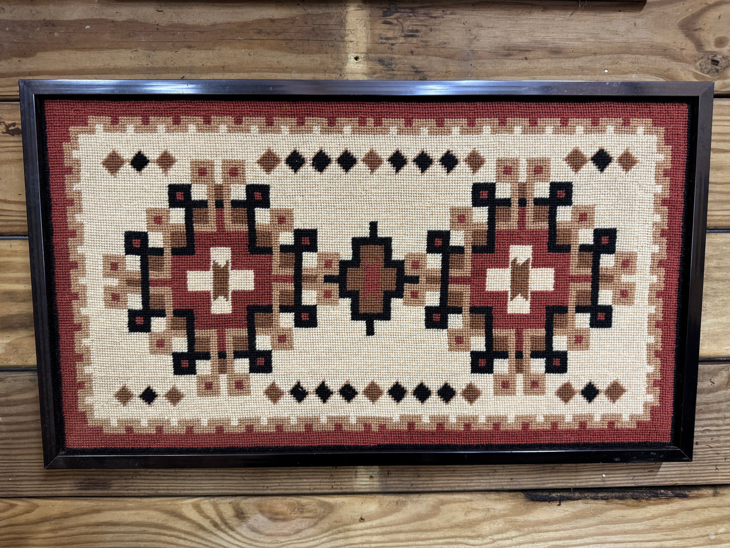 Framed needlepoint with geometric pattern on a wooden surface