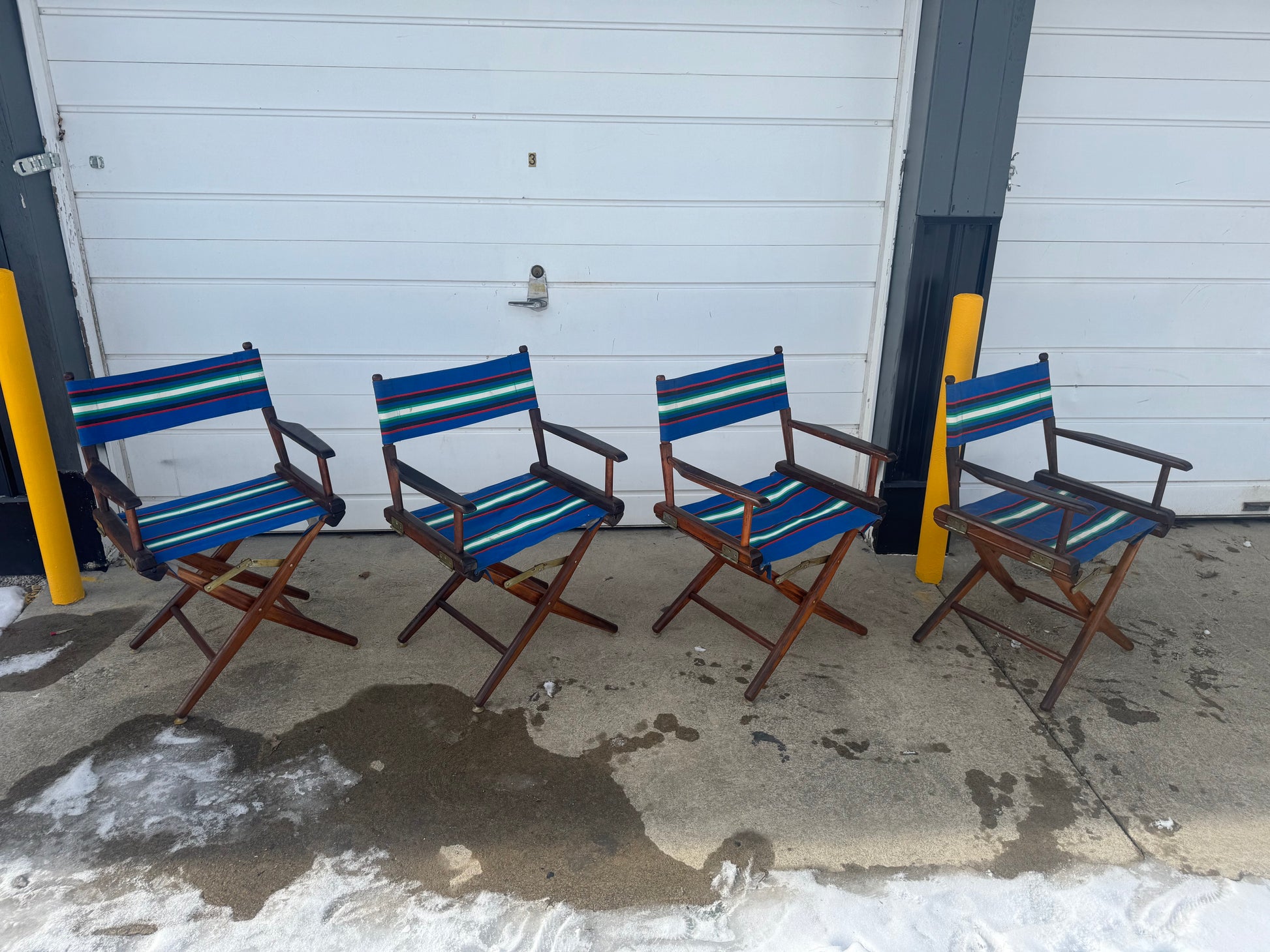 Four vintage canvas and wood folding captain's chairs placed outdoors, featuring a blue and white striped seat and backrest with a brown wood frame.