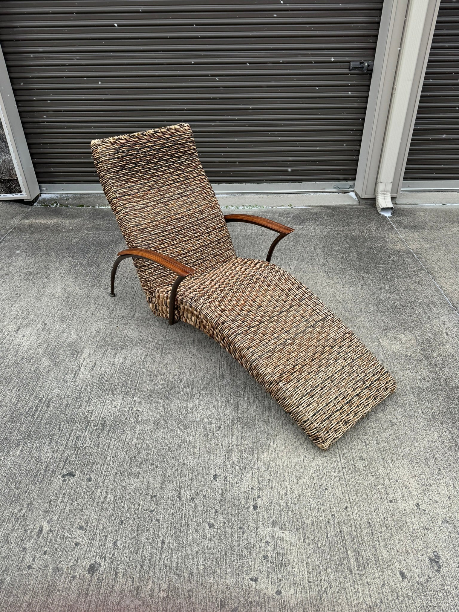 A beige wicker lounge chair with a metal frame, displayed on a concrete surface against a wall.
