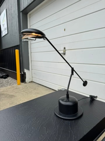 Black adjustable desk lamp on a black surface with a white wall and garage door in the background.
