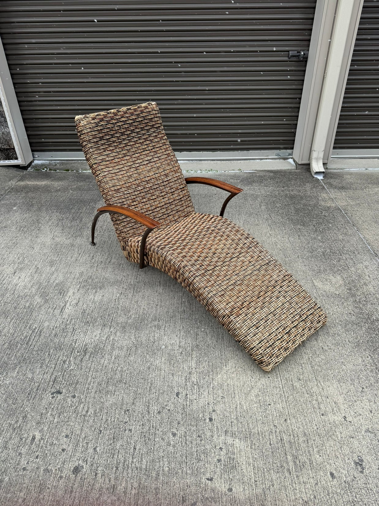 A beige wicker lounge chair with a metal frame, displayed on a concrete surface against a wall.