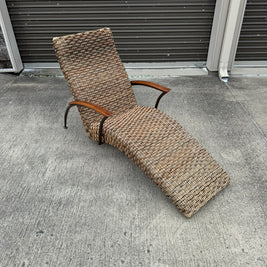 A beige wicker lounge chair with a metal frame, displayed on a concrete surface against a wall.